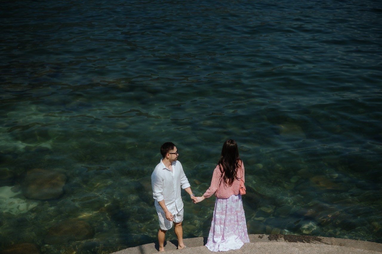 Kevin and Huỳnh holding hands at the water’s edge on Lake Como